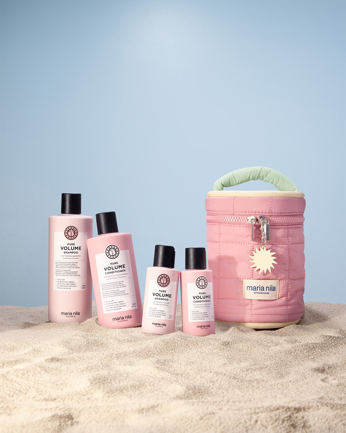 Set of hair care products with a pink Beauty Bag on a sandy surface and light blue background
