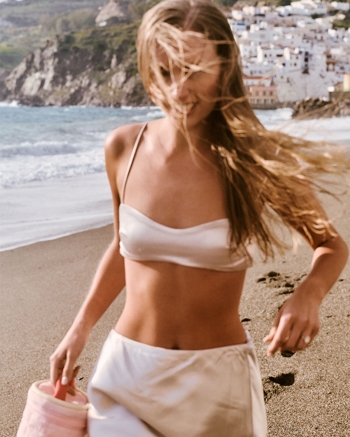 Woman in a bikini top walking on a beach with a scenic background