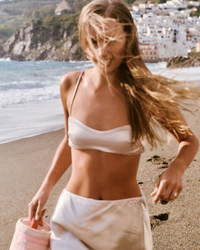 Woman in a bikini top walking on a beach with a scenic background