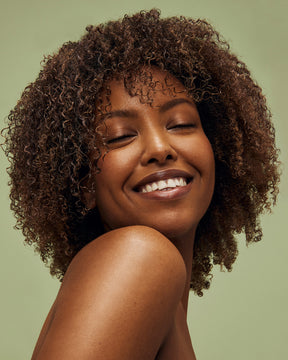Woman with curly hair smiling against a green background